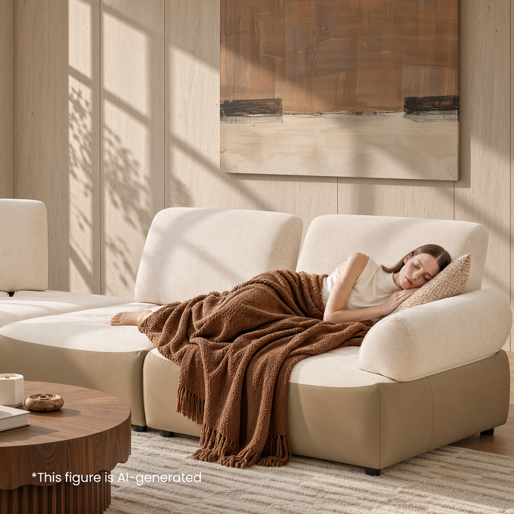 Woman sleeping under a brown blanket on a cream sectional sofa.