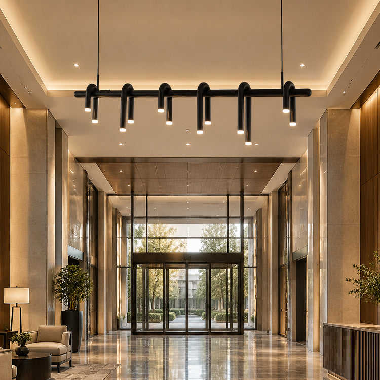 A modern lobby with a black ceiling light fixture, polished stone floor, seating, plants, and glass entrance doors.