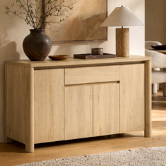 A light wood cabinet has four paneled doors, two central drawers, and slim warm-metal handles