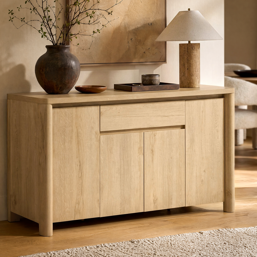 A light wood cabinet has four paneled doors, two central drawers, and slim warm-metal handles