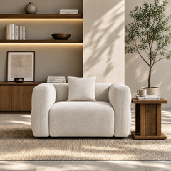 Cream upholstered armchair with rounded arms and a matching cushion in a sunlit room.