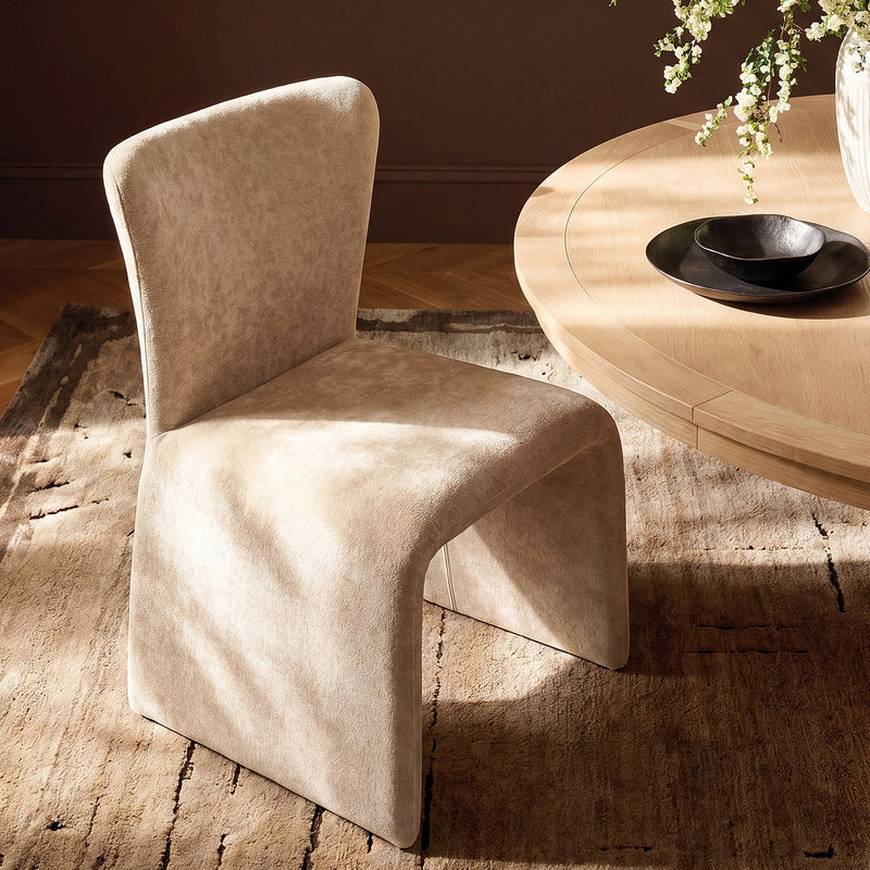 Light coffee upholstered dining chair with a curved U-shaped base beside a round table.