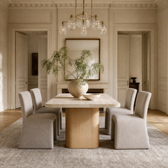 A dining room with a round pedestal table, four upholstered chairs, a leafy plant, and a glass pendant light.