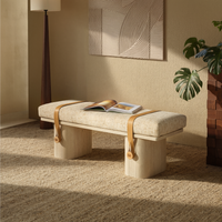 Beige upholstered bench with pale block legs, tan straps and an open book.