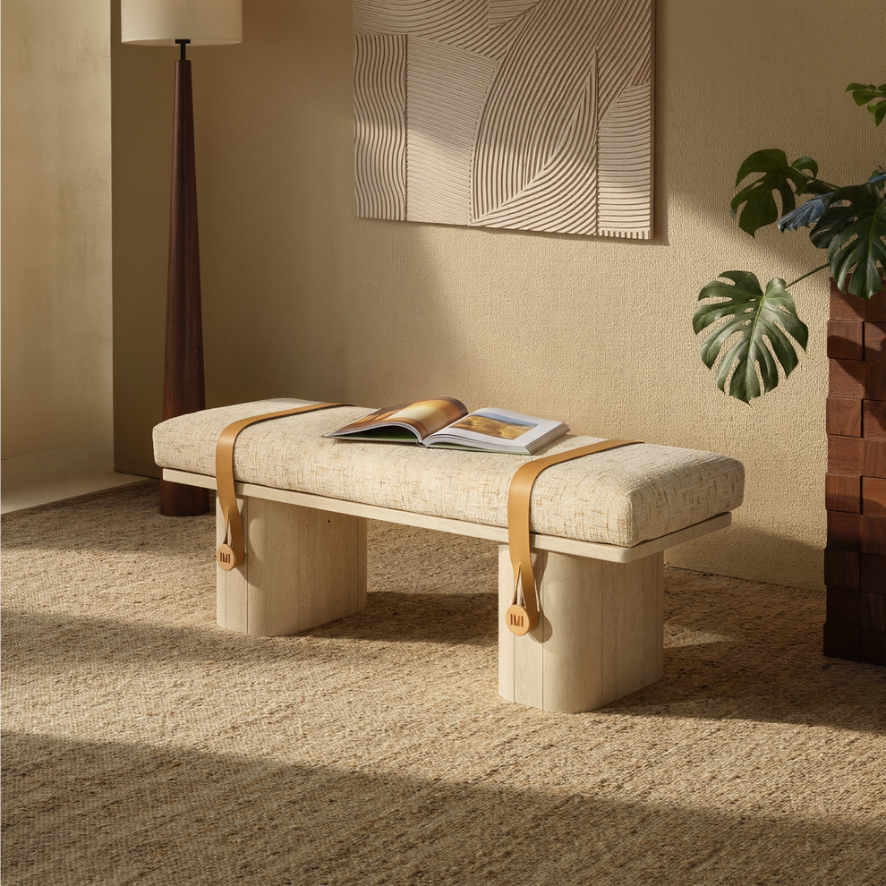 Beige upholstered bench with pale block legs, tan straps and an open book.