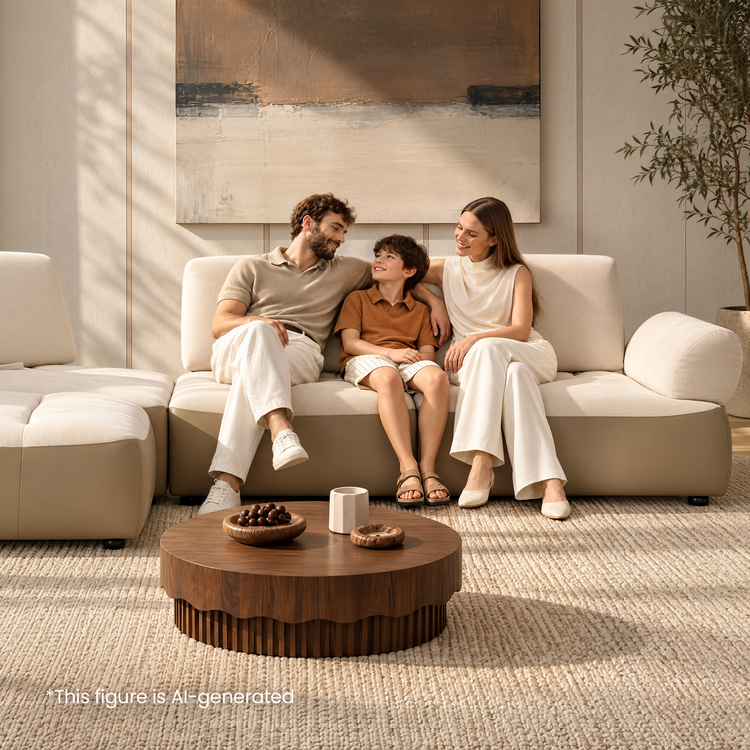Three people sit together on a cream sectional sofa in a sunlit living room.