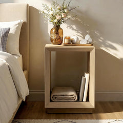 Light wood-tone nightstand with a tall open compartment holding books and a folded blanket beside a bed