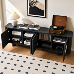 Black cabinet with open doors holds books, records and gaming equipment, with a record player, lamp, stacked books, candle and bowl on top beneath framed artwork.