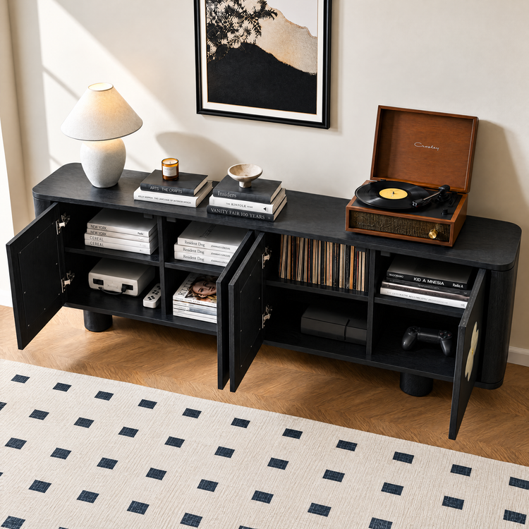 Black cabinet with open doors holds books, records and gaming equipment, with a record player, lamp, stacked books, candle and bowl on top beneath framed artwork.