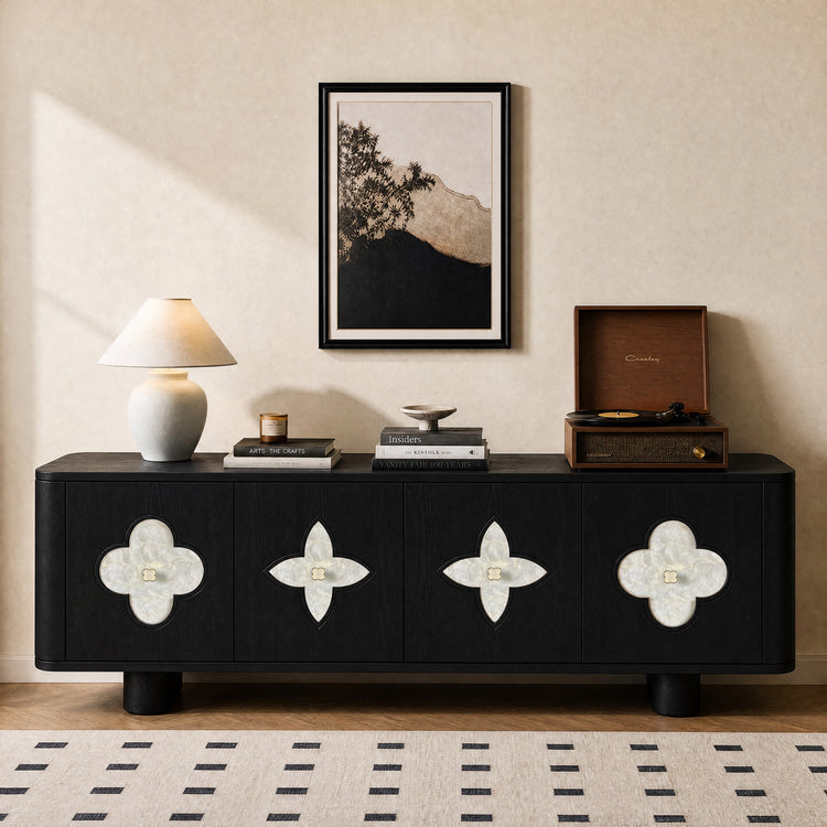 Black sideboard with four pale floral door motifs, topped with a cream lamp, books, a candle and an open record player beneath a framed abstract print.