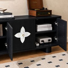 Black cabinet with open doors and a four-petal inlay holds books and a game console, with a wooden record player on top.