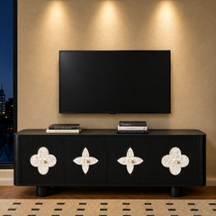 A black four-door cabinet with pale clover-shaped inlays stands beneath a blank wall-mounted television, with books on top and a city view through a window at left.