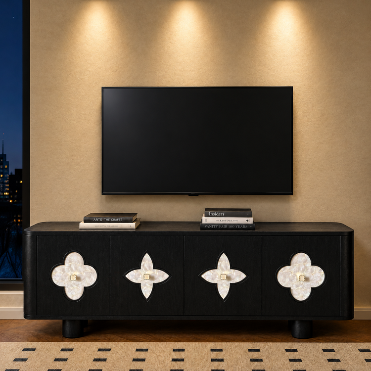 A black four-door cabinet with pale clover-shaped inlays stands beneath a blank wall-mounted television, with books on top and a city view through a window at left.