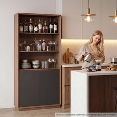 A woman pours water from a kettle into a coffee dripper beside a tall cabinet displaying bottles, glassware, and dishes.