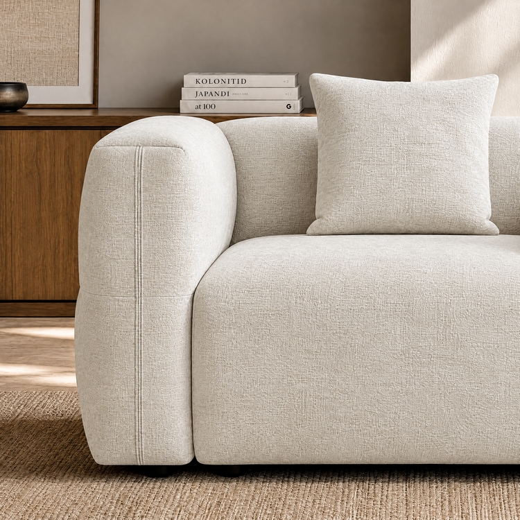 Close-up of a cream textured sofa with rounded arm and matching square cushion.