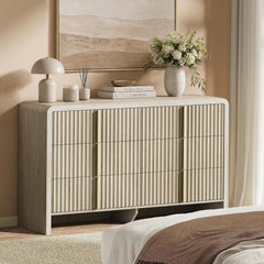 A nine-drawer cabinet with vertically fluted fronts and rounded outer edges is styled with books, a lamp, and flowers