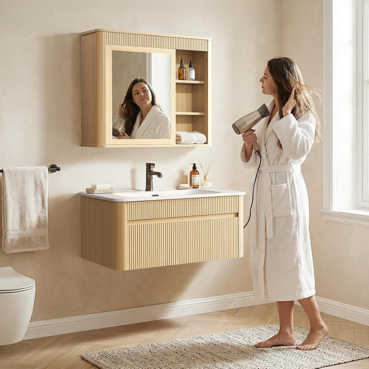 Woman drying her hair beside a floating fluted vanity with a white sink and matching mirror cabinet with open side shelves