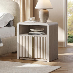 Whitewashed nightstand with two fluted drawers, an open cubby and rounded upper corners beside a bed