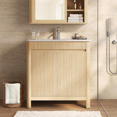 Light wood-tone bathroom vanity with a white sink top and vertically fluted front beside a glass shower enclosure