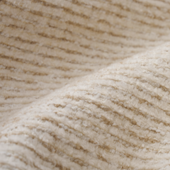 Close-up of a cream-colored fuzzy textile with dense, wavy fibers and ridged rows.