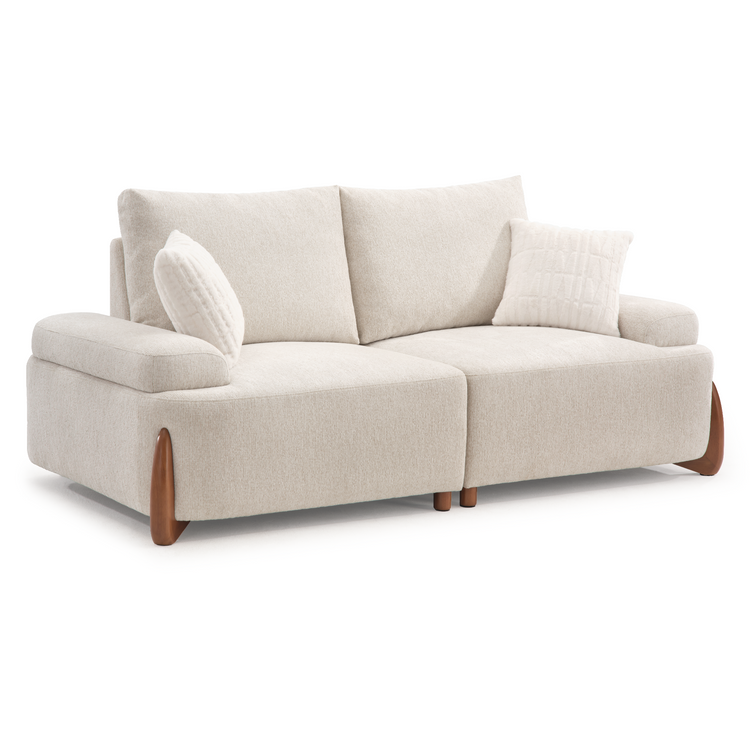 A light beige two-seat sofa with two back cushions, two white throw pillows, broad arms, and curved brown legs, shown against a white background.