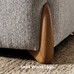 Close-up of a curved brown furniture leg with visible grain beside textured gray upholstery, resting on a beige patterned rug.