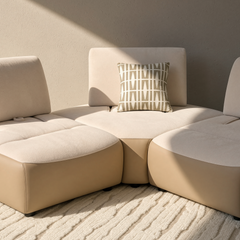 Cream modular sectional sofa with curved seats and a patterned pillow in sunlight.