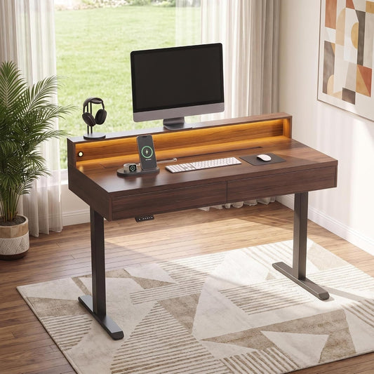 A dark wood desk with a raised back shelf and black metal legs holds a monitor, phone on a charging stand, keyboard, mouse, and headphones.