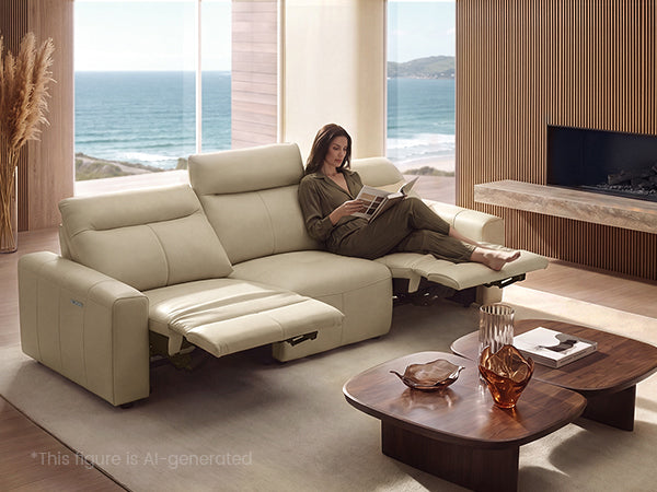 Woman reading on a beige reclining sofa in an oceanfront living room.