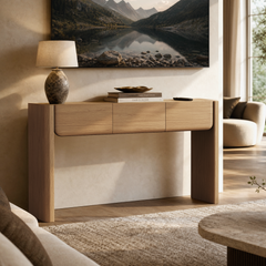 A light wood-tone console table has three rounded-front drawers and two thick slab legs