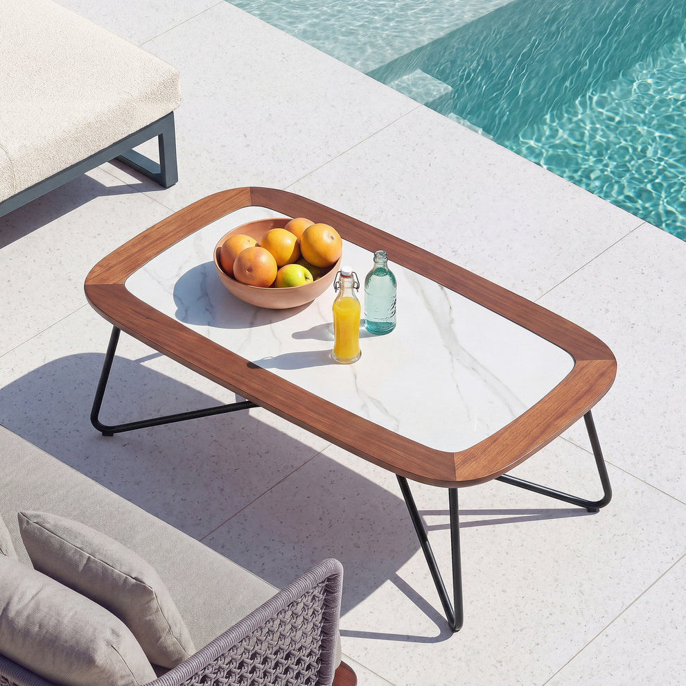 Rounded outdoor coffee table with a pale patterned top and black sled legs