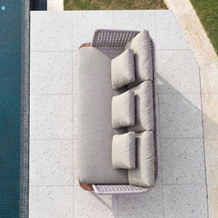 Top-down view of a gray cushioned outdoor sofa with woven side panels on pale paving