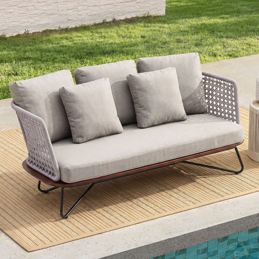 Grey outdoor loveseat with patterned woven sides, a brown base and dark angled legs on a poolside rug