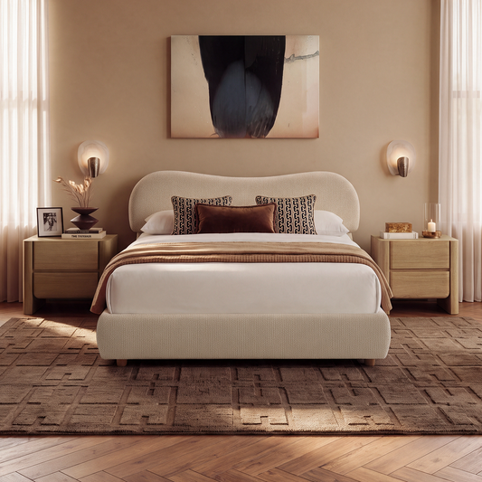 A bedroom with a cream upholstered bed, patterned pillows, wooden bedside tables, wall sconces, and abstract artwork above the headboard.