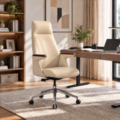 Cream high-back office chair with dark brown armrest tops and a silver wheeled base beside a desk with a laptop, open book and potted plant in a sunlit room.