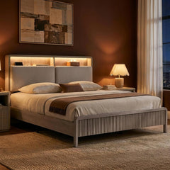 A bedroom with a low bed featuring a ribbed footboard and upholstered headboard, layered neutral bedding, and a lit bedside lamp.