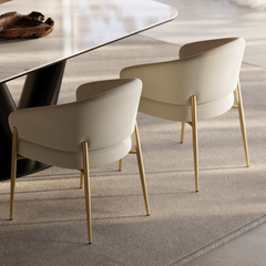 Two cream upholstered dining chairs with gold-tone legs beside a modern table