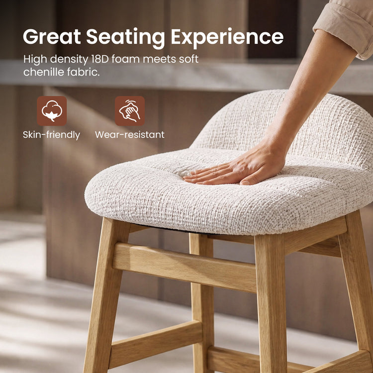 A hand presses into the textured cream seat cushion of a stool with a curved upholstered back, light brown legs and crossbars.