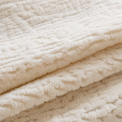 Close-up of cream-colored fabric folded into layers, with a raised, plush geometric pattern and recessed lines.
