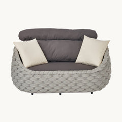 A gray woven loveseat appears frontally with dark cushions, Two cream throw pillows rest against the back