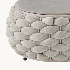 A close-up shows a round tabletop above a basket-weave body formed by thick braided strands
