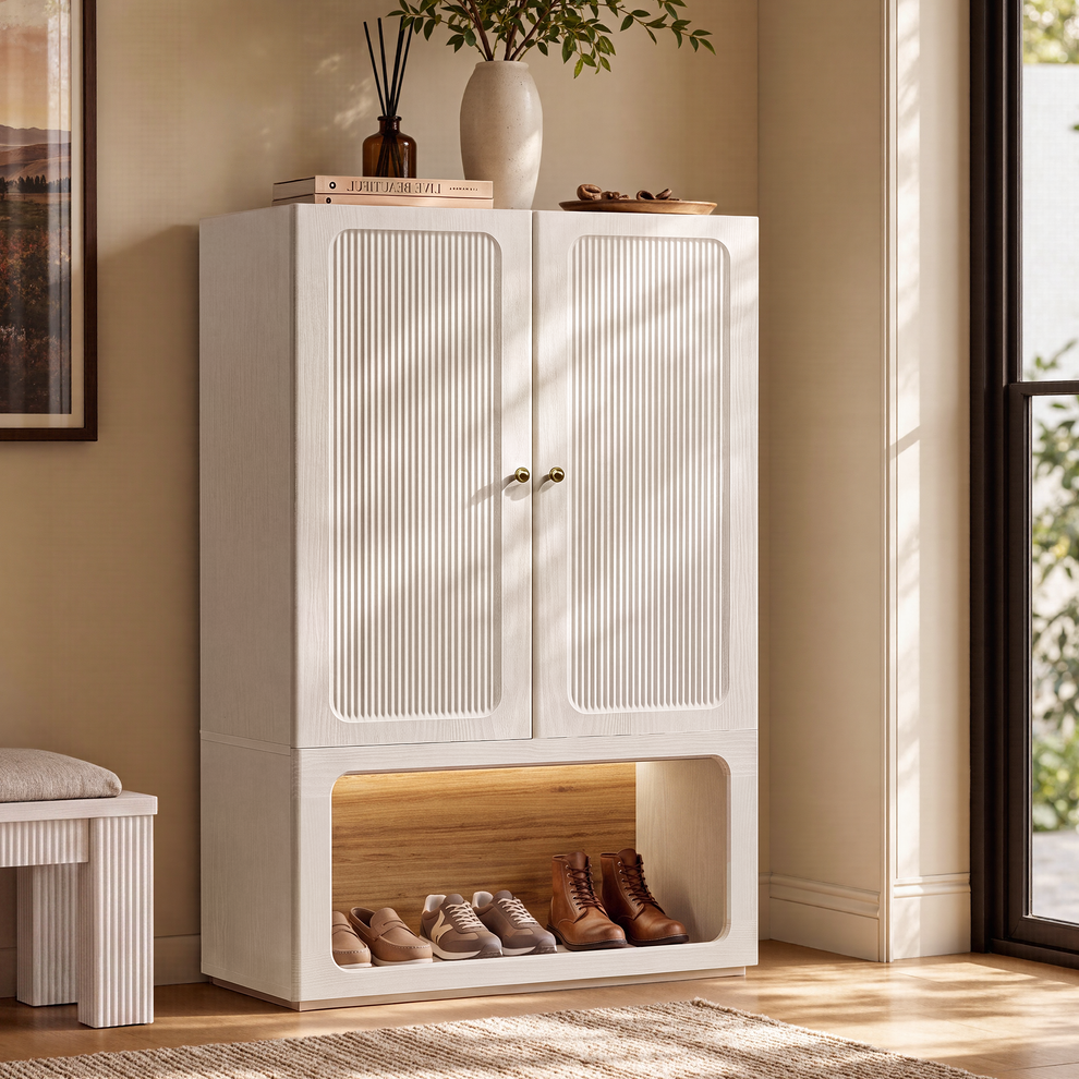 White shoe cabinet with fluted double doors and an open lower compartment holding shoes beside an entryway window