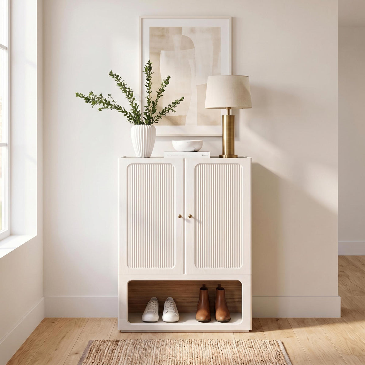 White shoe cabinet with ribbed double doors and open shelf, styled in a bright entryway.