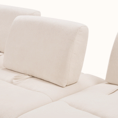 Close-up of cream upholstered sofa cushions with rounded backrests and stitched seams.