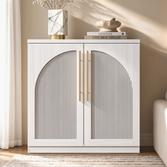 White accent cabinet with fluted double doors forming a broad arch and long gold-tone handles beside a sofa