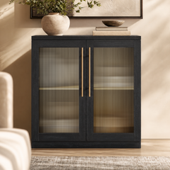 Black two-door cabinet with ribbed translucent panels and long gold-tone handles in a furnished room