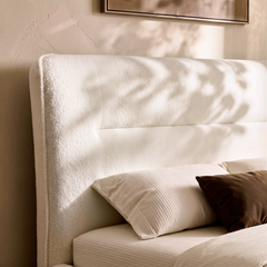 Cream upholstered headboard has a nubby texture and horizontal inset seam, Striped and brown pillows rest against it