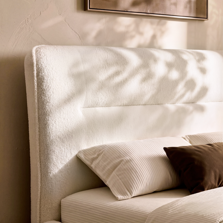 Cream upholstered headboard has a nubby texture and horizontal inset seam, Striped and brown pillows rest against it