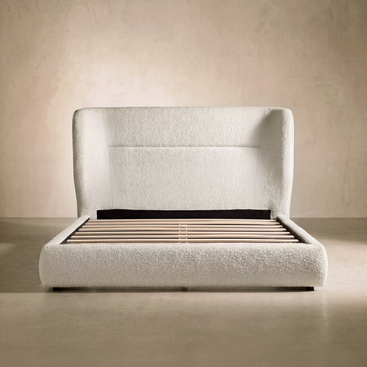 Ivory textured bed frame has a tall rounded upholstered headboard, Pale slats span the open mattress platform