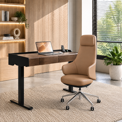 Tan high-back office chair with a wheeled base beside a brown desk with black legs, a laptop and phone, surrounded by illuminated shelves, plants and a window with blinds.